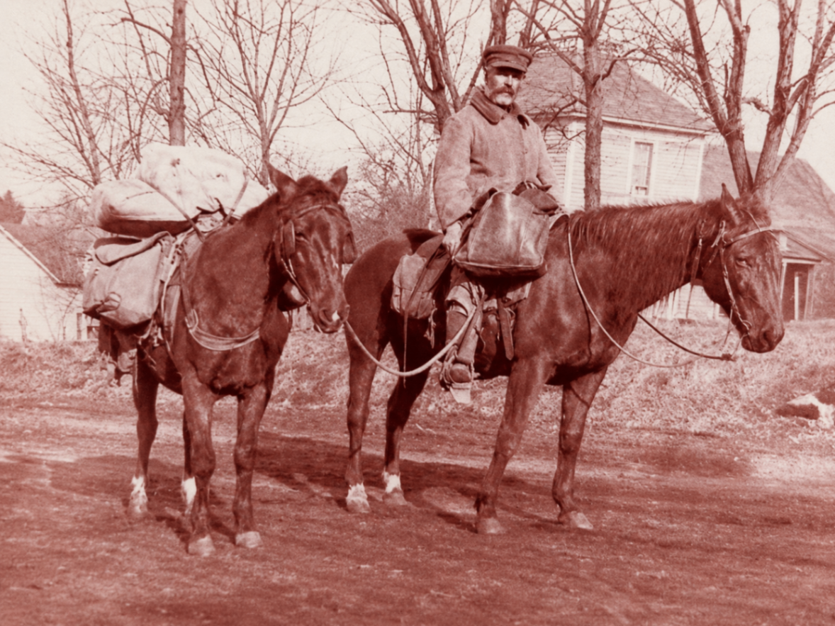 Rural mail carrier on horseback leading a second horse loaded with mail sacks