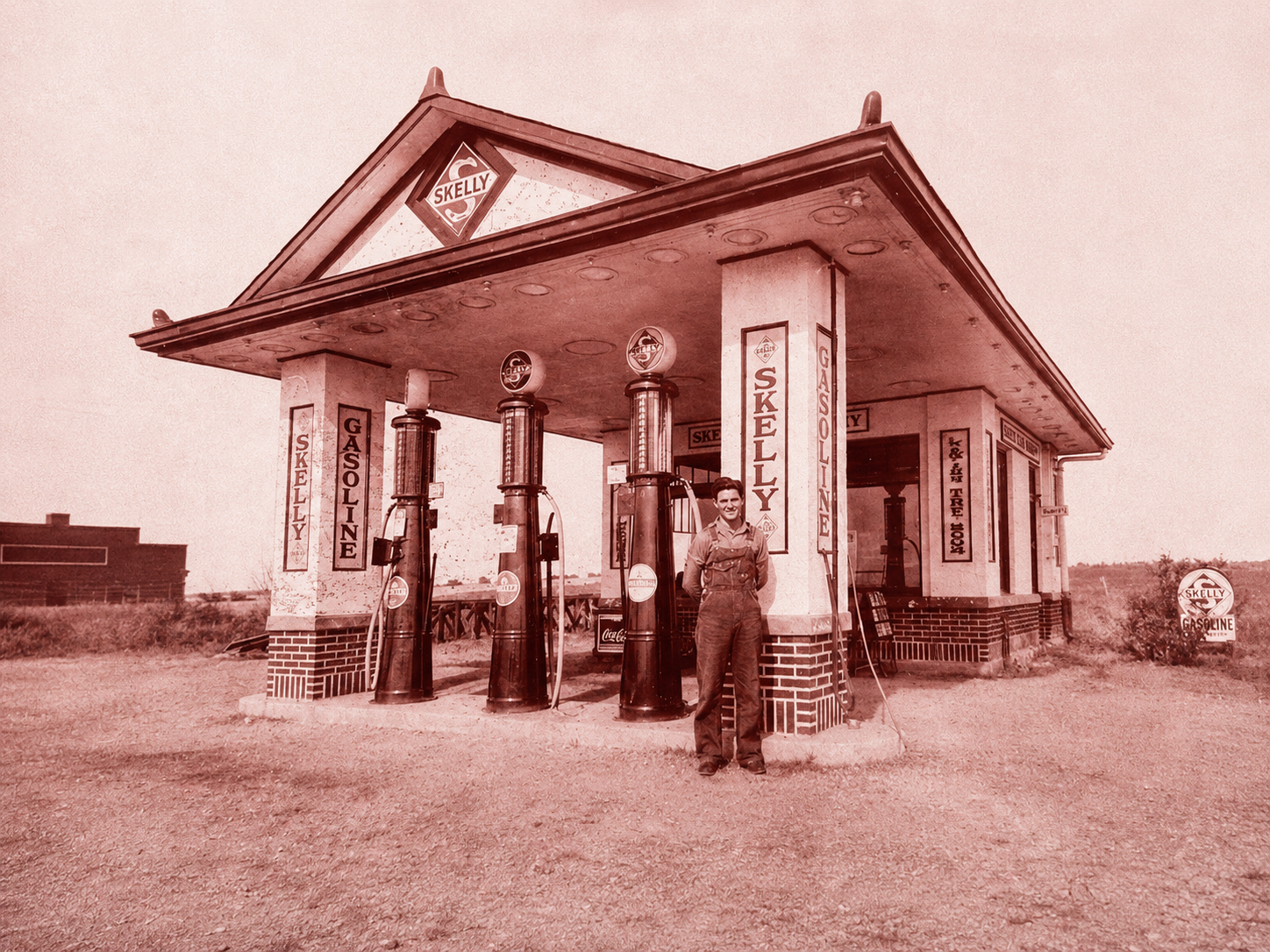 Attendant in overalls standing beside three visible-glass pumps at a Skelly gasoline station