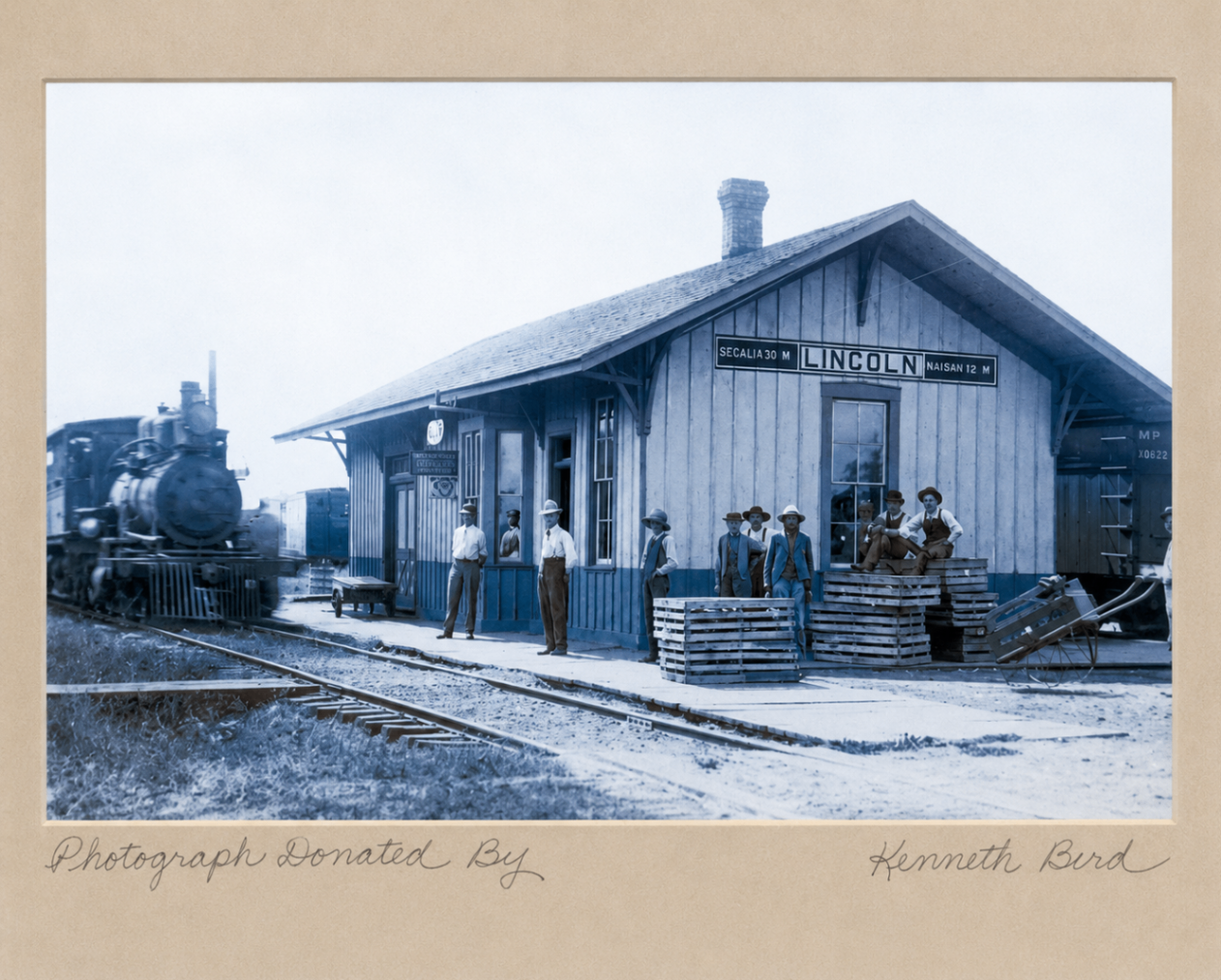 Steam locomotive at the Lincoln, Missouri railroad depot with workers on the platform